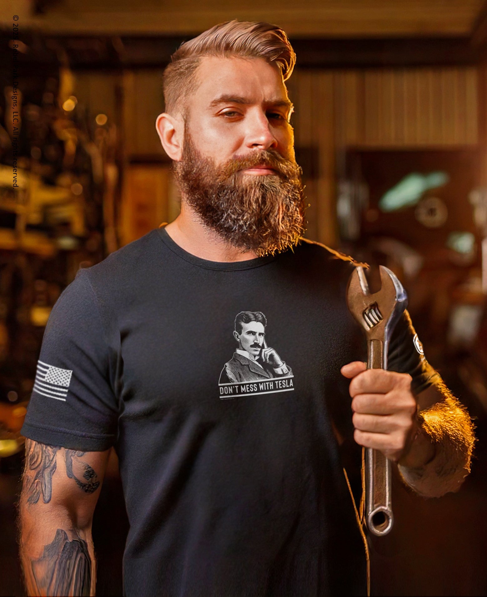 Man wearing a black t-shirt with a graphic design, holding a wrench in a workshop setting.