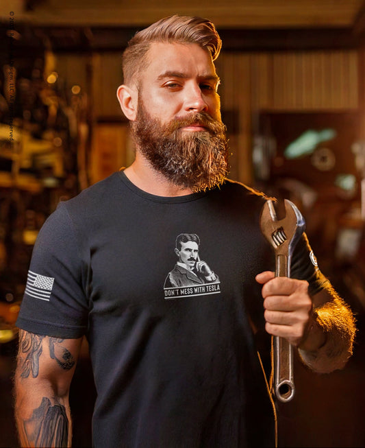 Man wearing a black t-shirt with a graphic design, holding a wrench in a workshop setting.