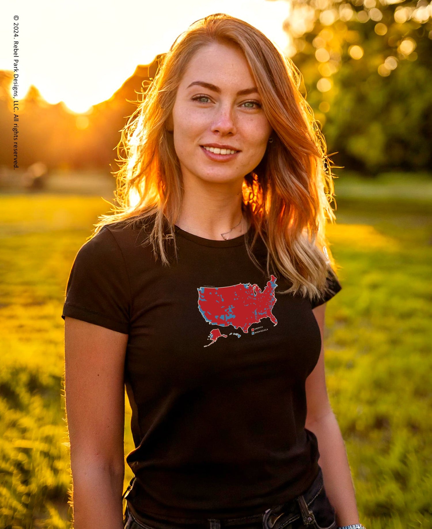 Woman wearing a black t-shirt with a graphic design, standing in a field with sunset lighting.