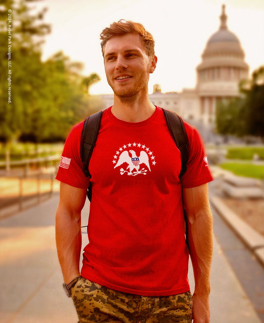 Man wearing a red t-shirt with a logo in front of the U.S. Capitol building.