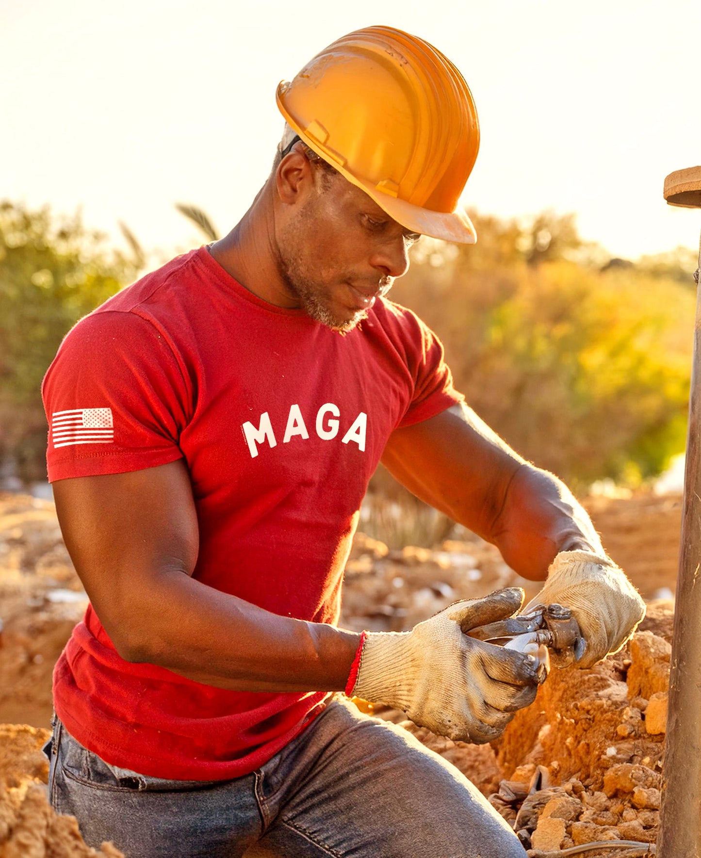 Person wearing a red 'MAGA' shirt and orange hard hat working outdoors.