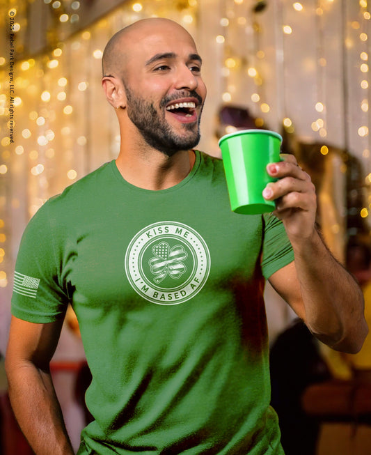 Man wearing a green t-shirt with a logo and text, holding a green cup against a blurred indoor background.