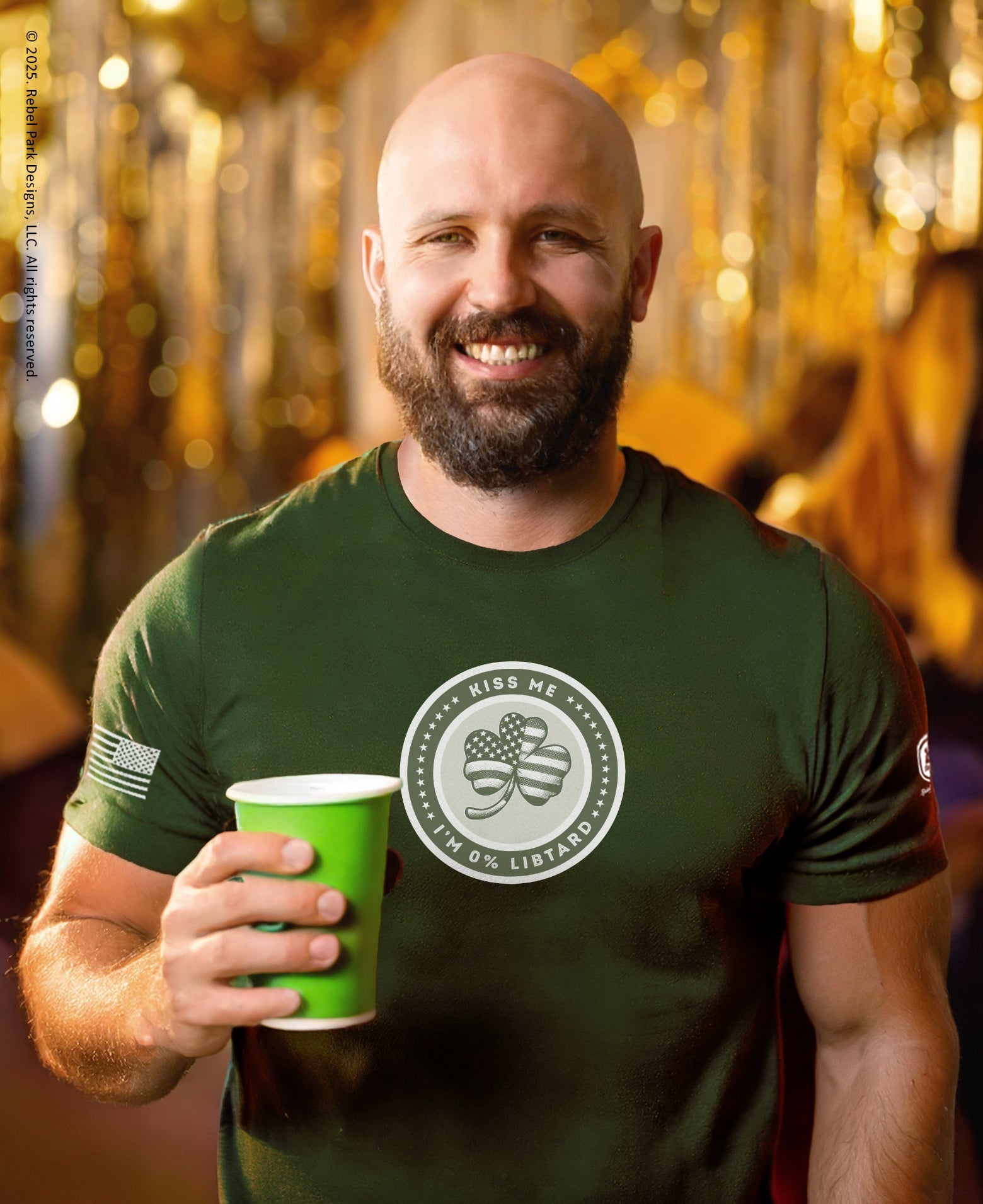 Man wearing a green t-shirt with a logo, holding a green cup against a blurred background.