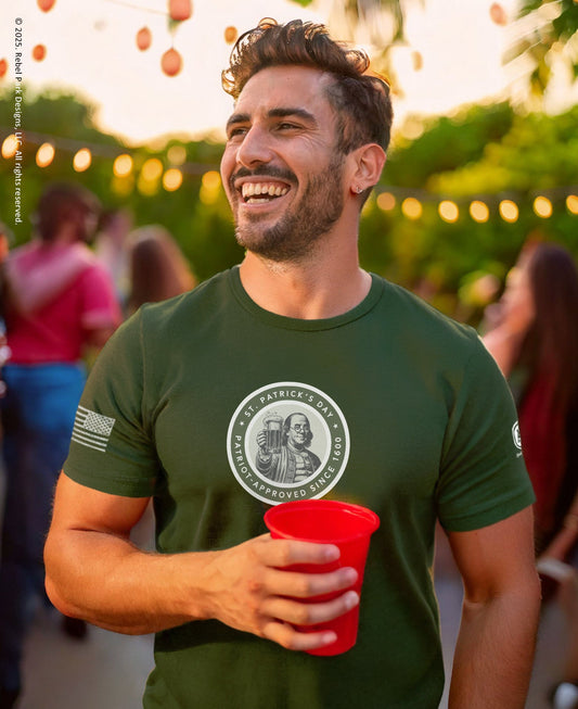 Man wearing a green t-shirt with a logo, holding a red cup, in a festive outdoor setting.