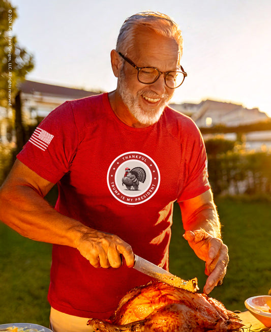 Man in a red t-shirt carving a turkey outdoors during sunset.