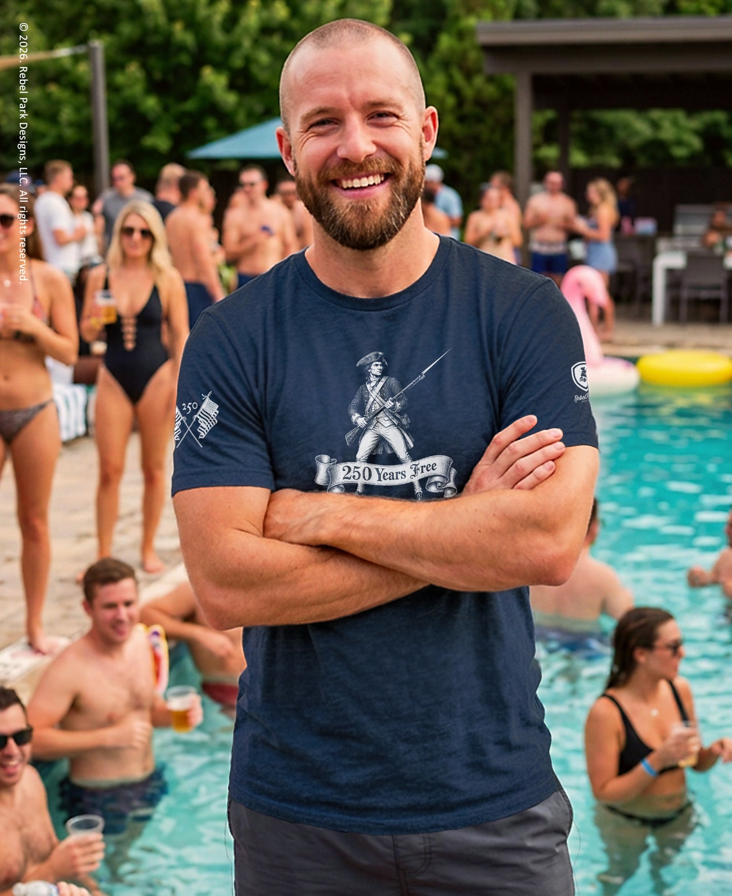 Man standing by a pool with people around, wearing a navy blue t-shirt with graphics and text.