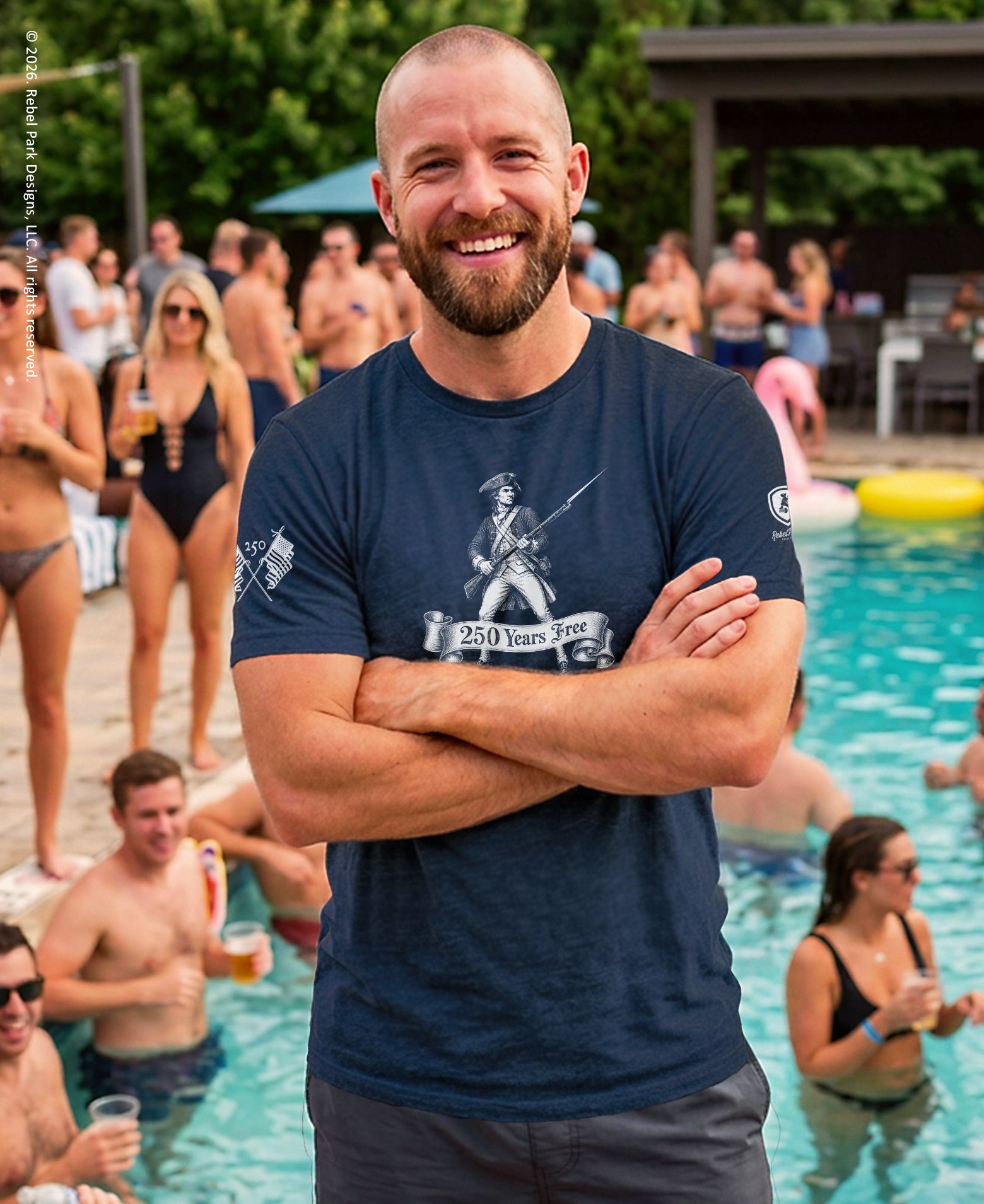 Man standing by a pool with people around, wearing a navy blue t-shirt with graphics and text.
