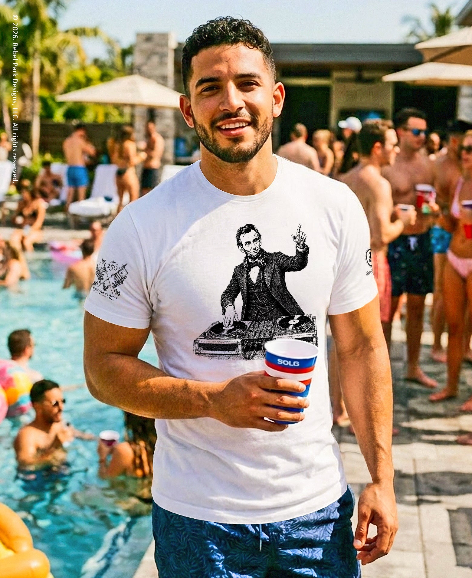 Man wearing a white t-shirt with a graphic design by a poolside with people in the background.