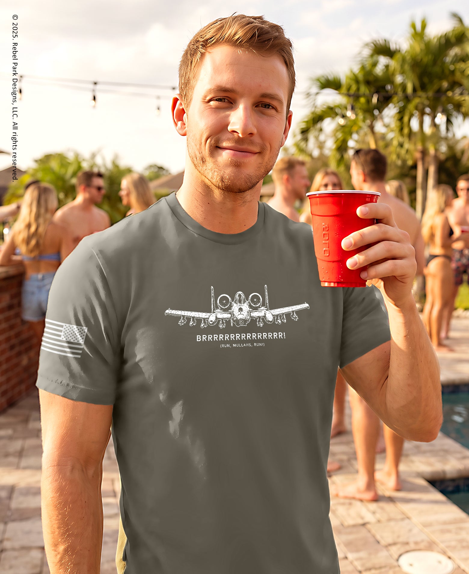 A man at a pool party wearing a dark gray graphic t-shirt with a white printed design and holding a red plastic cup.