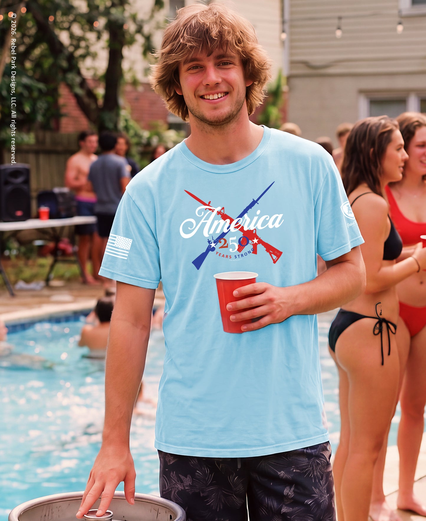 Man in a light blue t-shirt with 'America' design holding a red cup by a poolside.