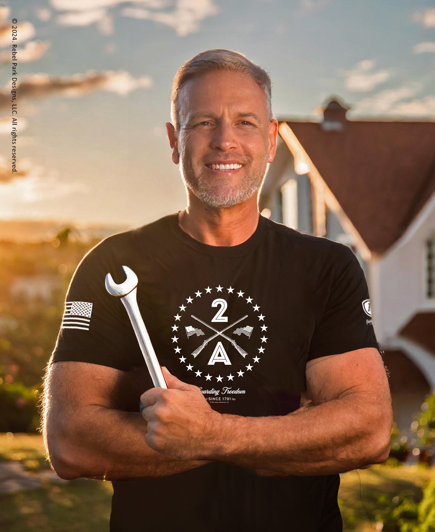 Man wearing a black t-shirt with a logo and holding a wrench, standing outdoors.