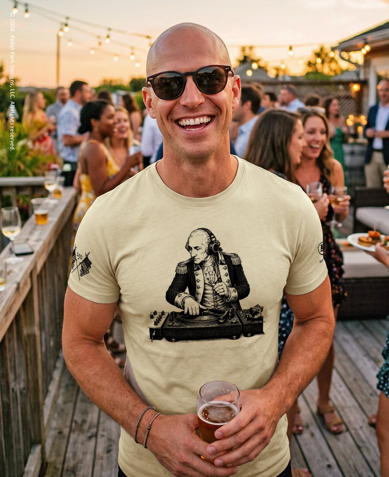 Man wearing a t-shirt with a graphic design, holding a drink, at an outdoor social event.