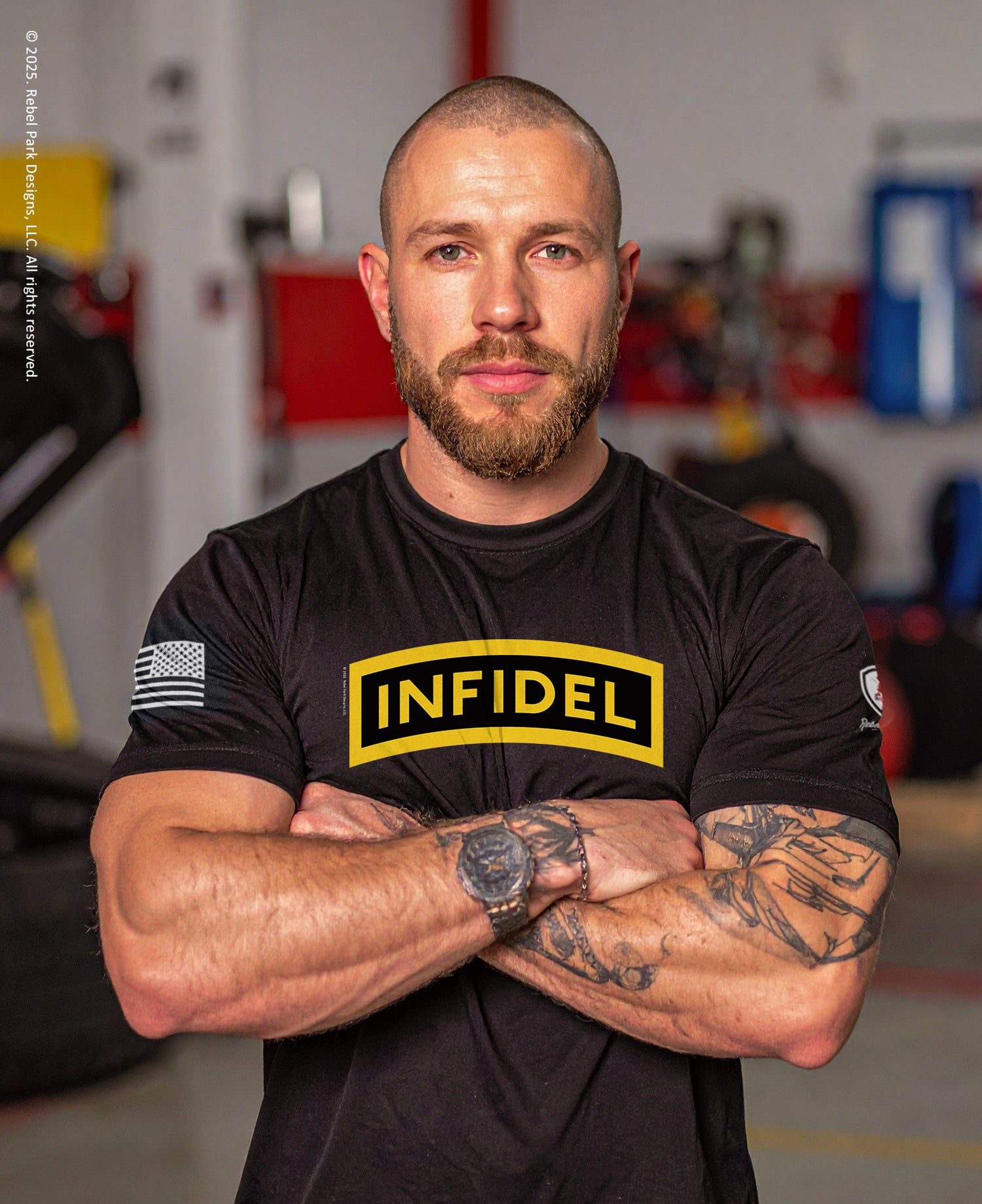 Man wearing a black t-shirt with 'INFIDEL' logo in a garage setting