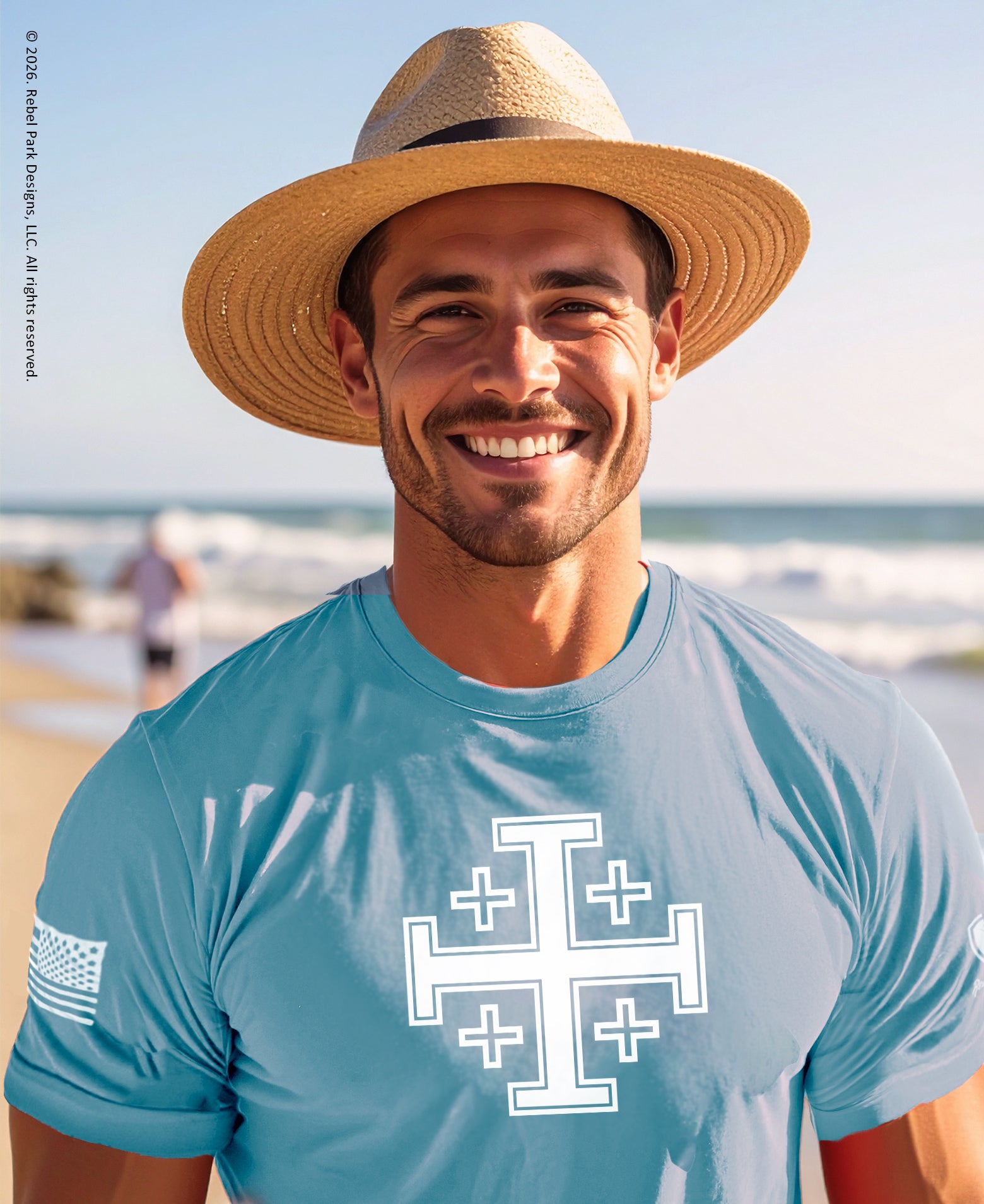 Man wearing a straw hat and blue t-shirt with a white logo on a beach.
