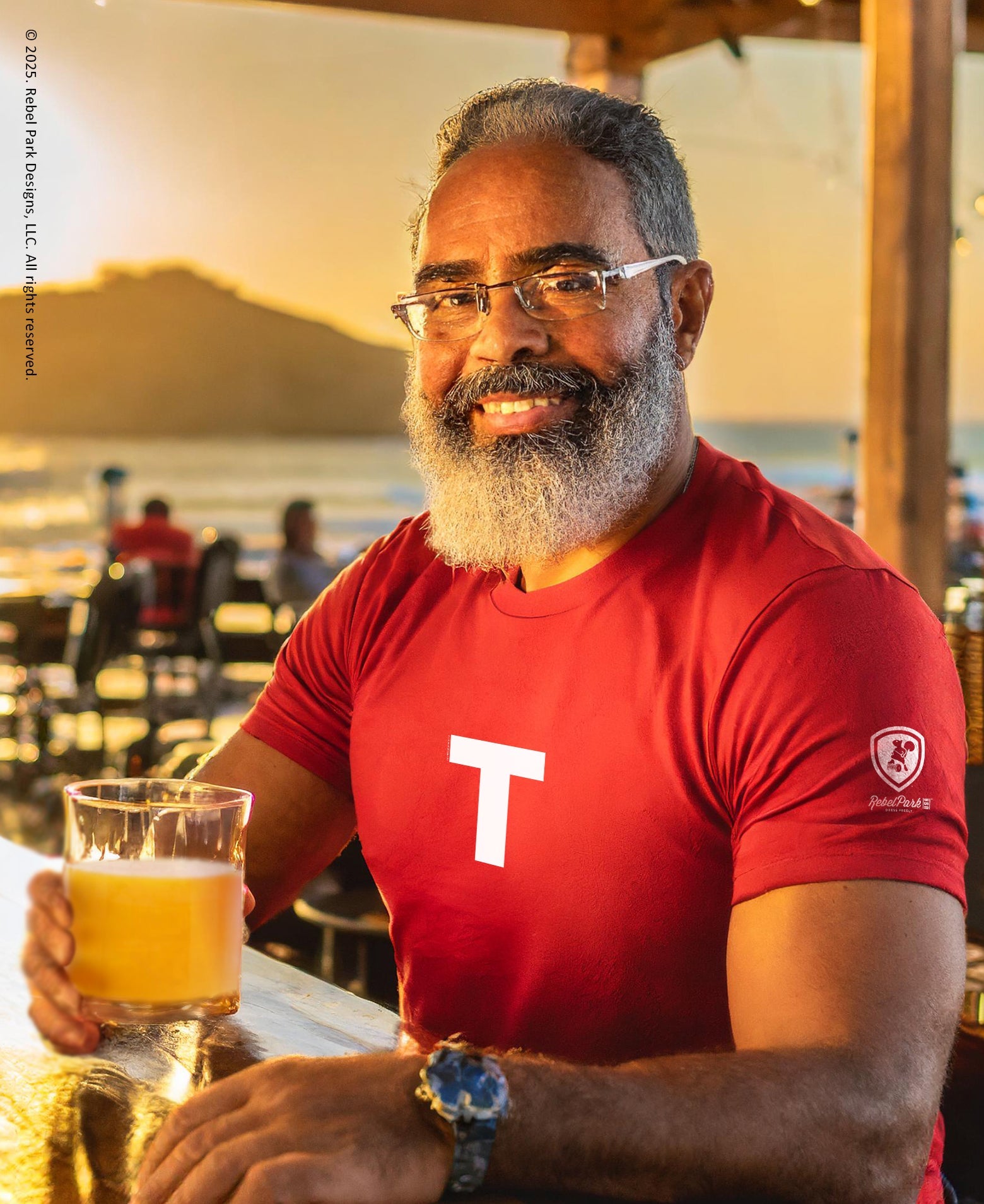 Man in a red shirt with a 'T' holding a glass of beer outdoors