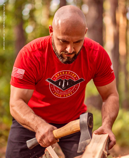 Man in a red t-shirt with a logo chopping wood outdoors