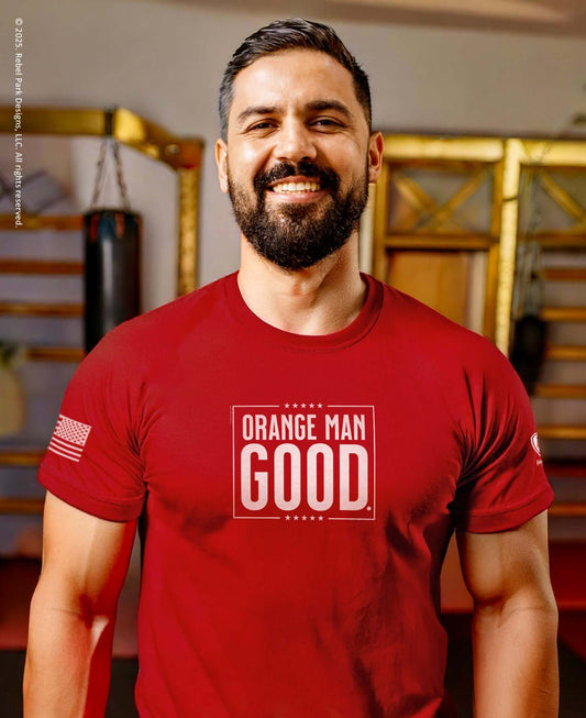 Man in red 'Orange Man Good' T-shirt, smiling confidently in a gym setting, showcasing patriotic style.