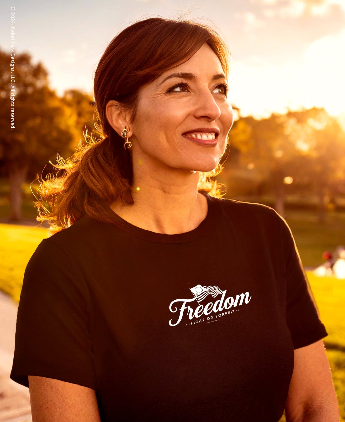 Woman wearing a black t-shirt with 'Freedom' logo outdoors during sunset.