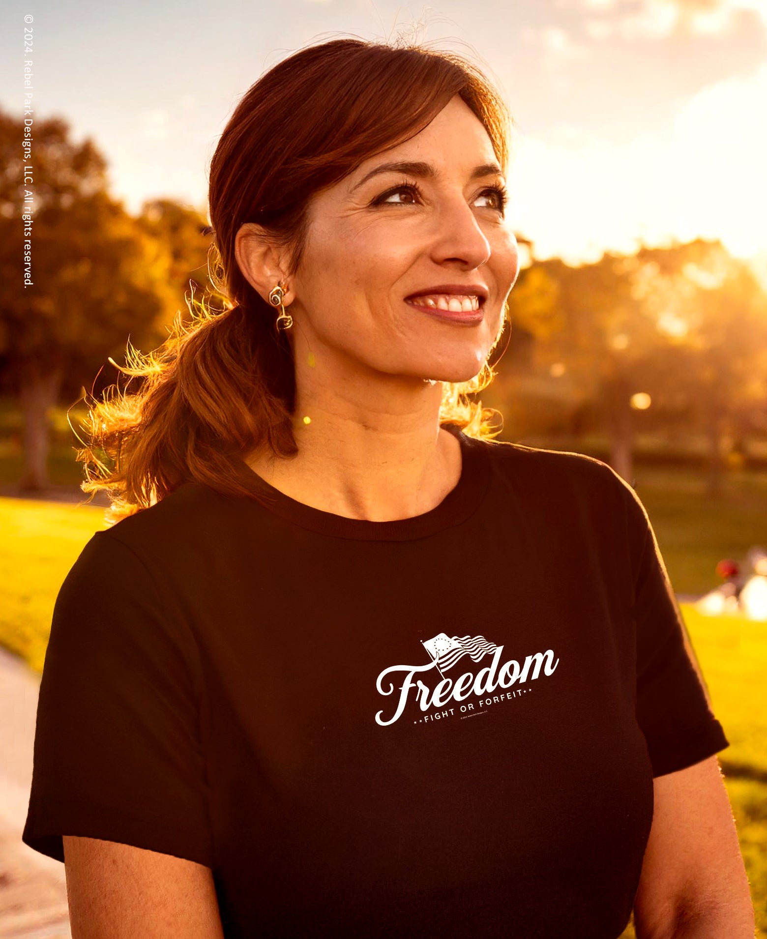 Woman wearing a black t-shirt with 'Freedom' logo outdoors during sunset.