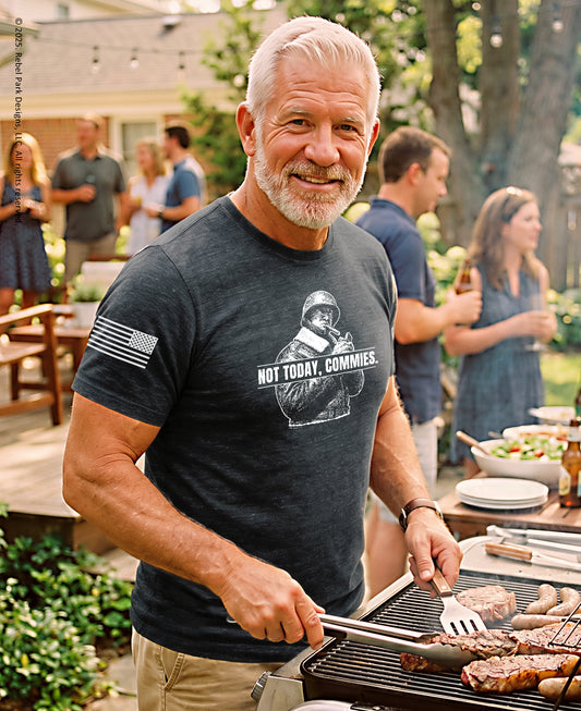 A smiling man with white hair and a beard grilling outdoors on a barbecue while wearing a dark charcoal heathered t-shirt with a graphic of a soldier holding a rifle and the text 'THE TRUTH WILL SET YOU FREE'.