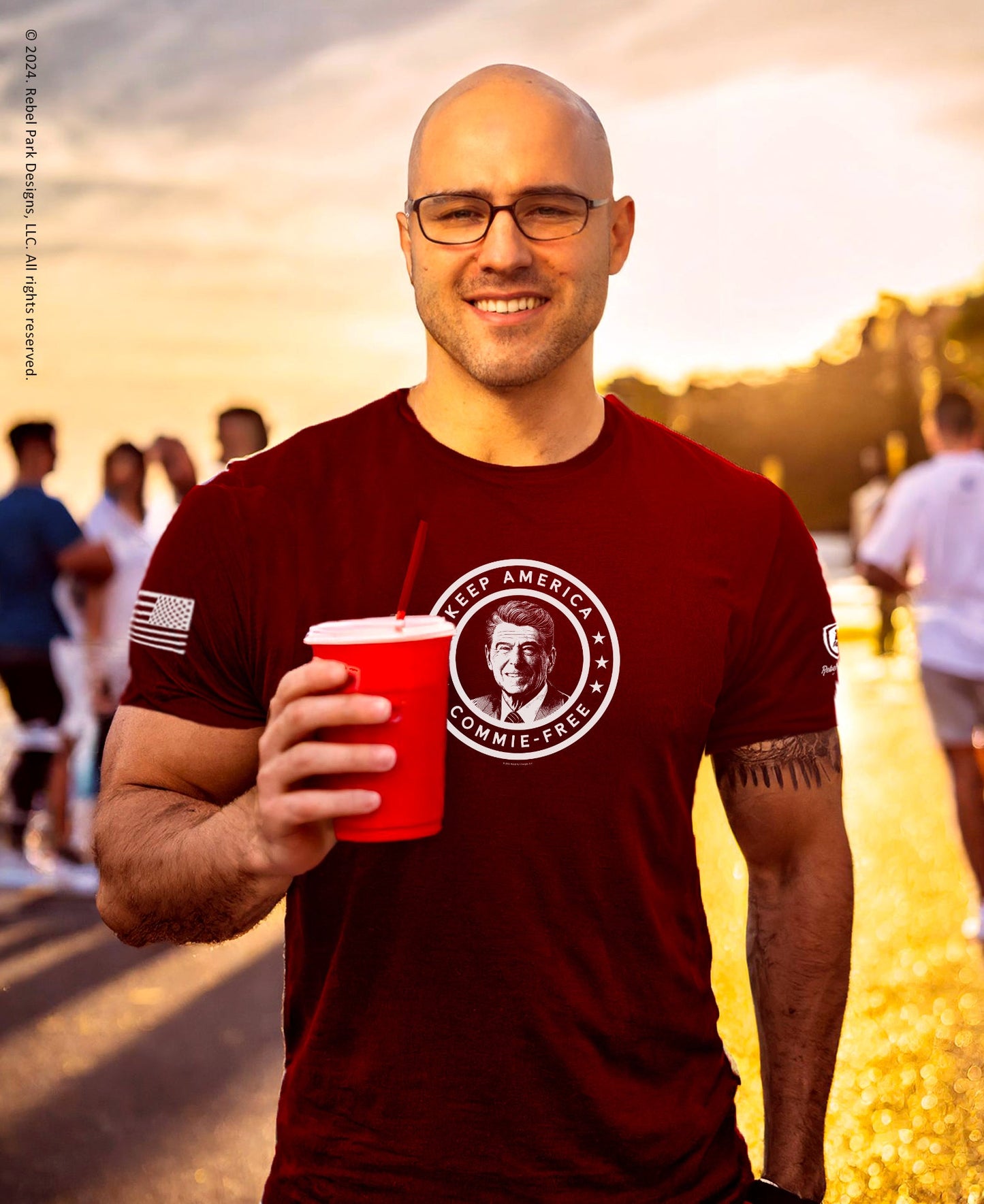 Man wearing a red t-shirt with a graphic design, holding a red cup outdoors.
