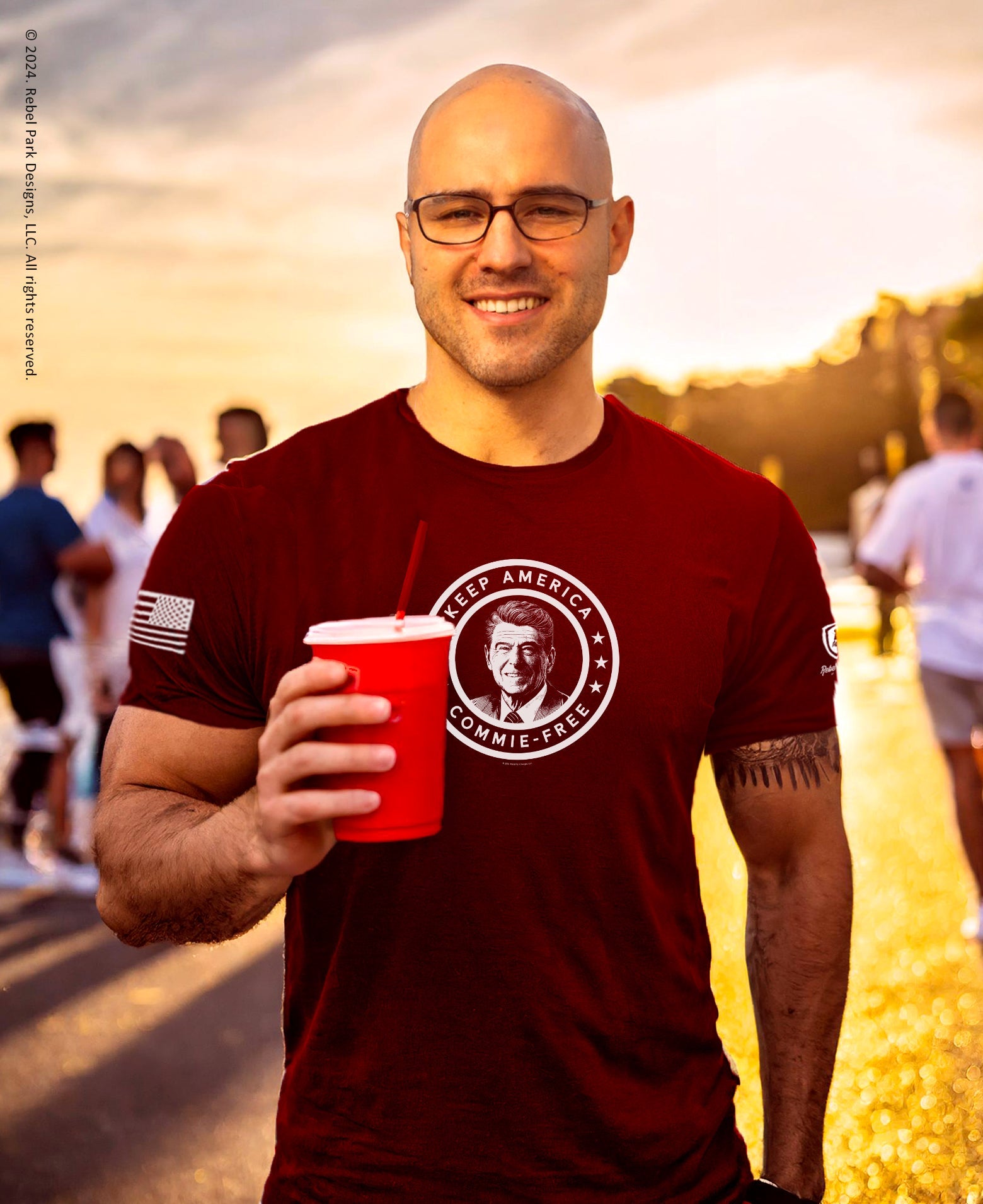 Man wearing a red t-shirt with a graphic design, holding a red cup outdoors.