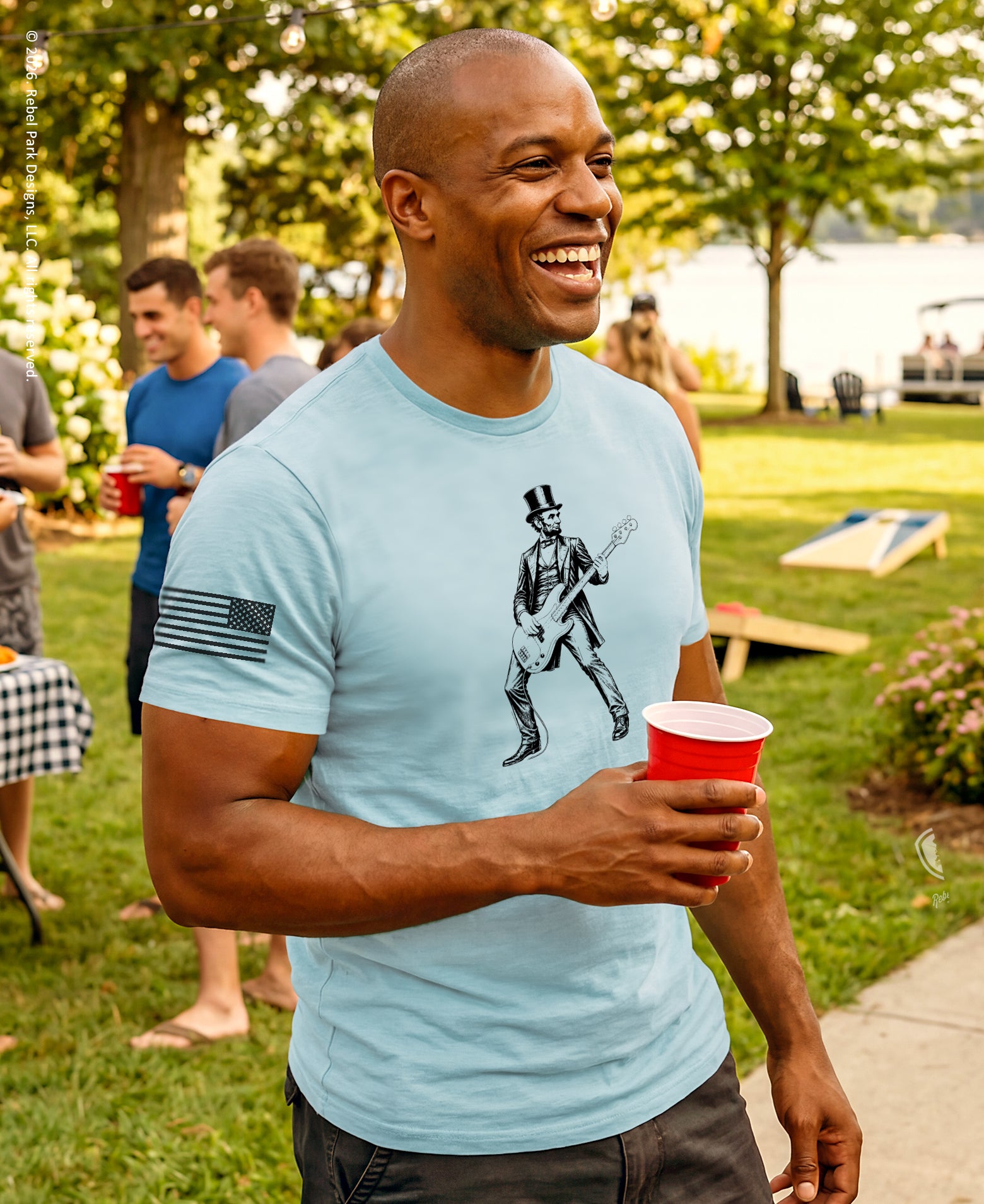 Man in light blue t-shirt with graphic design holding a red cup outdoors
