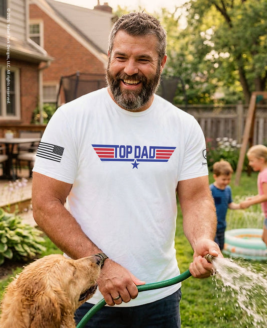 Man wearing a 'Top Dad' t-shirt, holding a hose with a dog and children in a backyard.