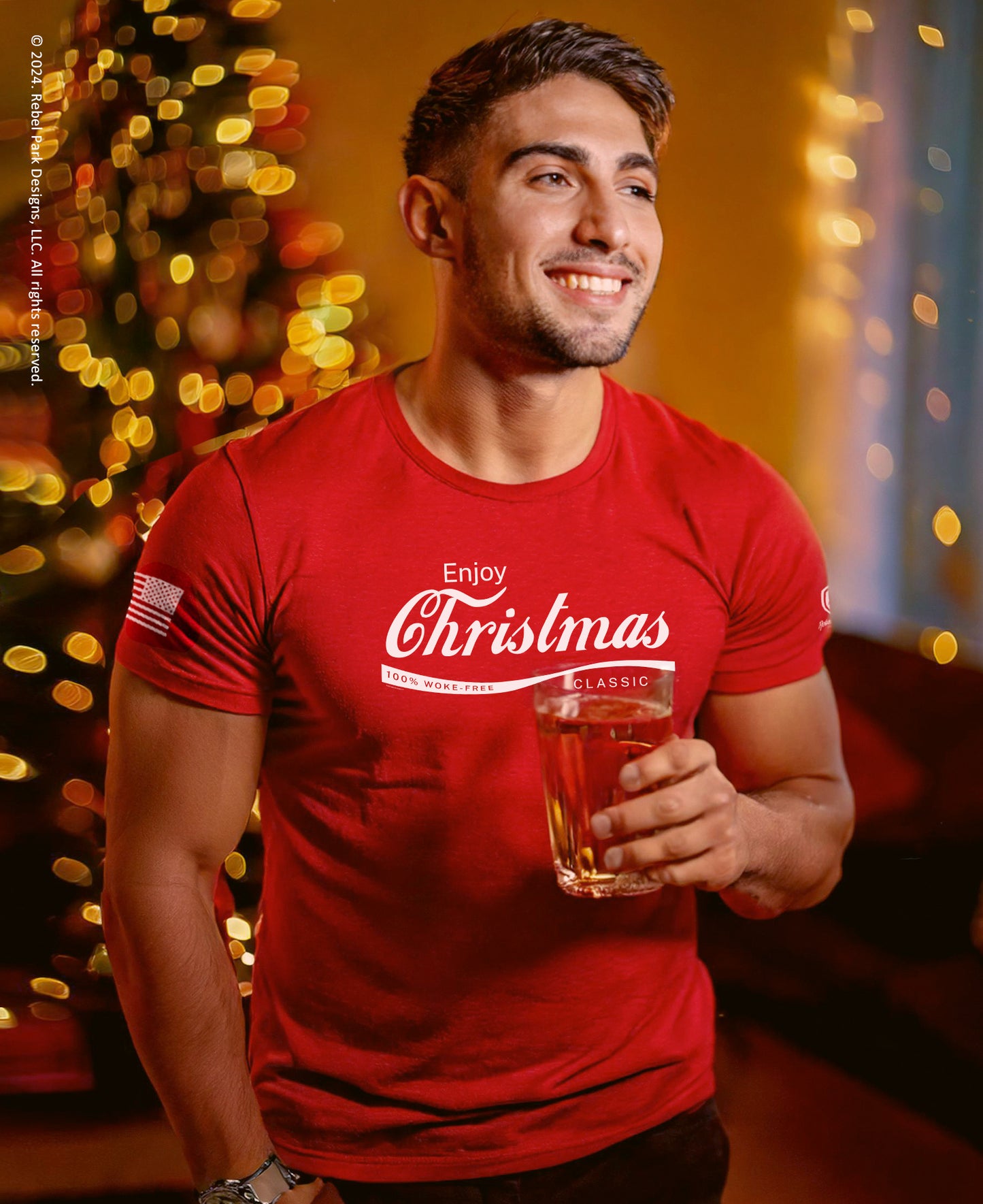 Man wearing a red 'Enjoy Christmas' shirt holding a glass of beer with a festive background.